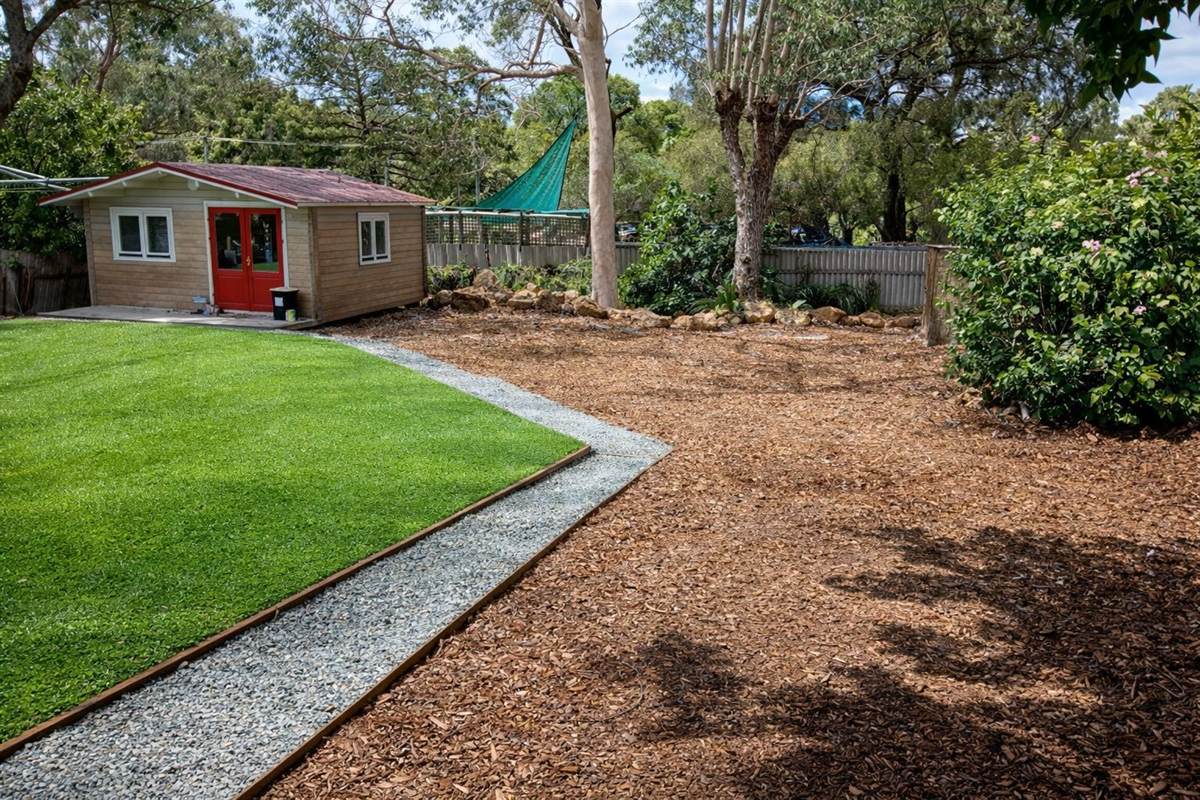 Back yard after: fresh lawn, mulch and river-rock edging, weatherboard cottage in background